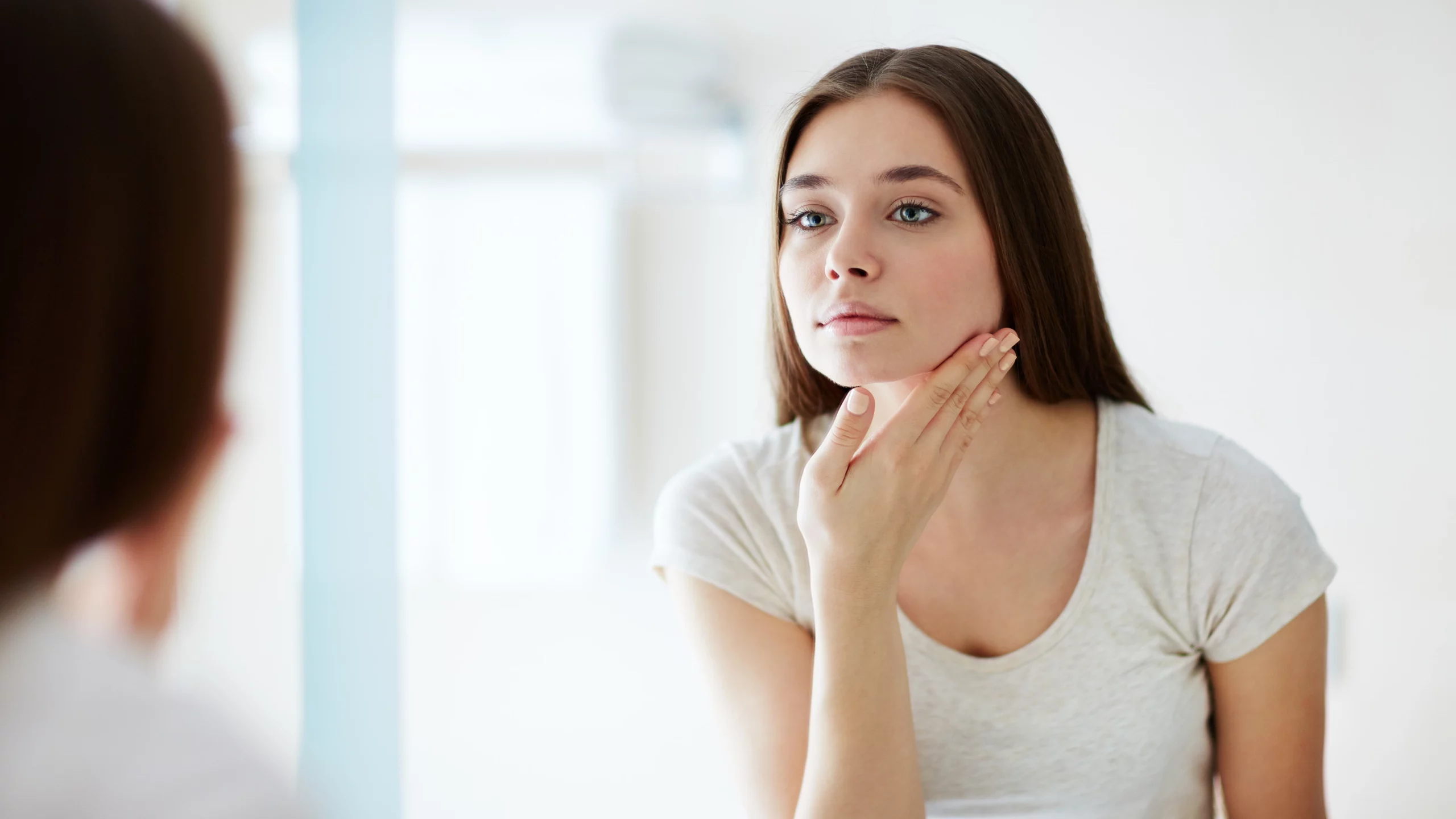 Young woman looking in the mirror and touching her jaw.