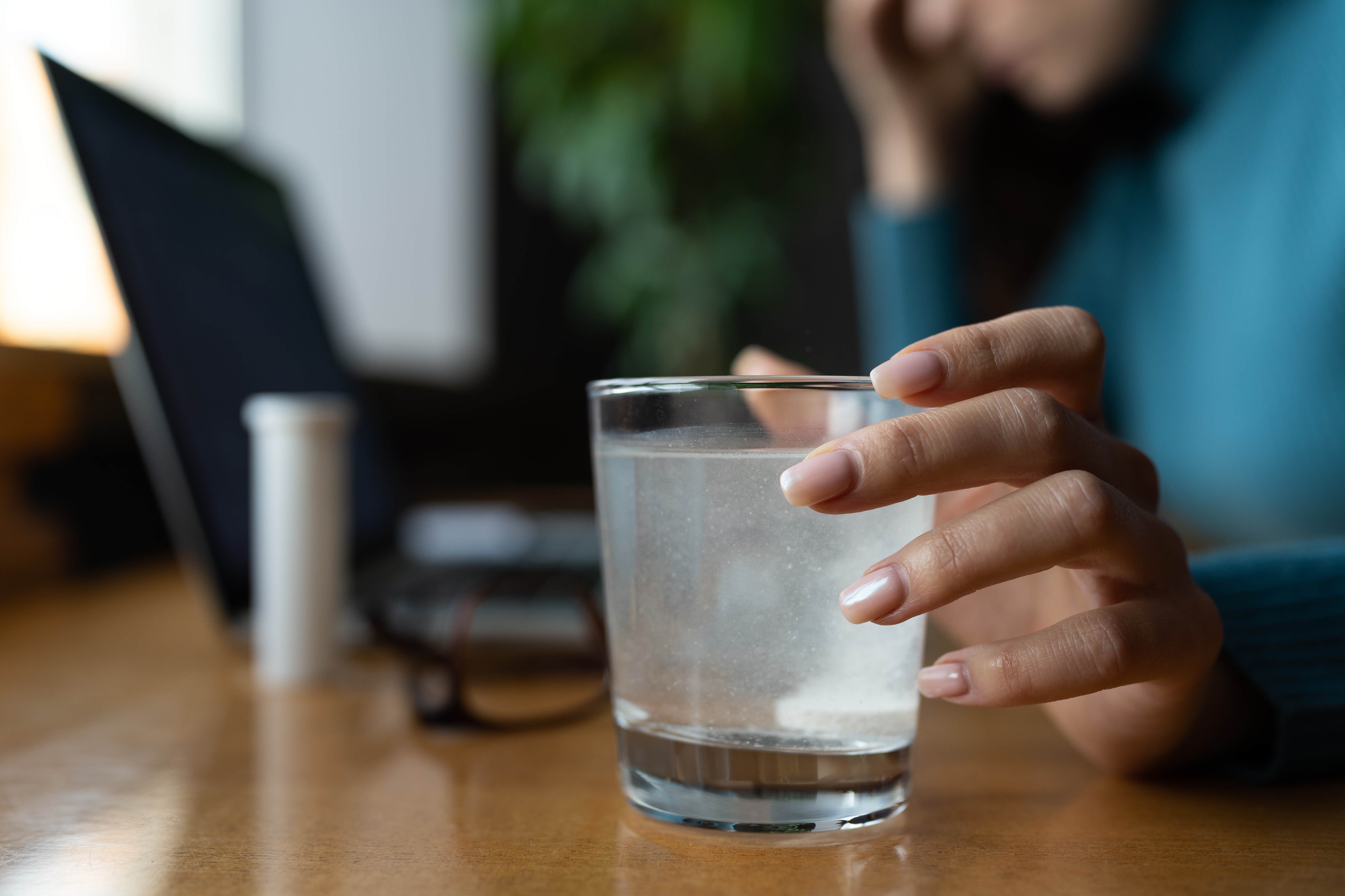 A tablet in a cup of water with woman in background working on a computer